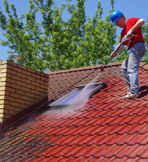 House roof cleaning with pressure tool. Worker on top of building washing tile with professional equipment. Moss removing with water.